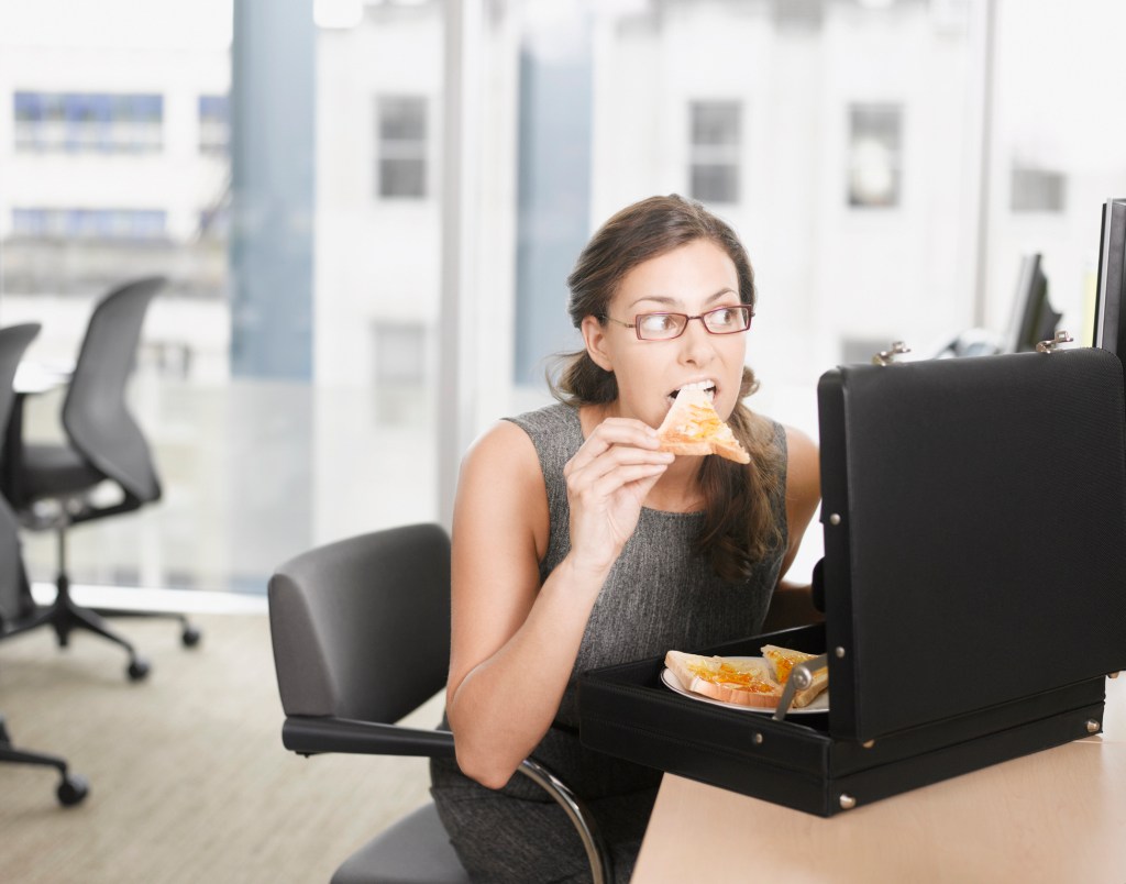 Businesswoman eating a slice of pizza from her briefcase