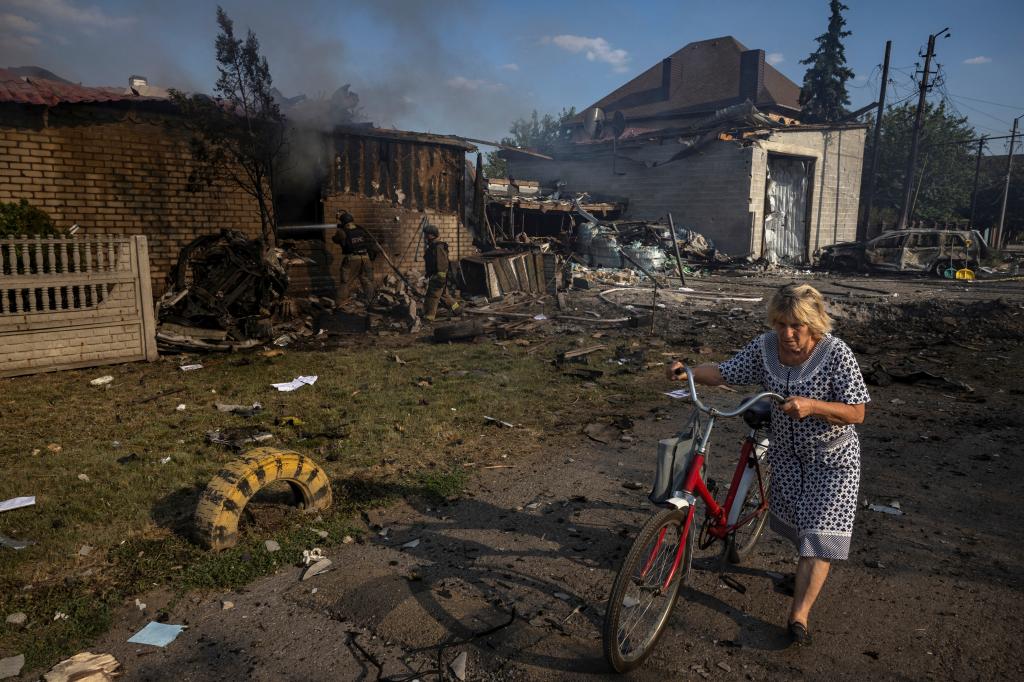 A Ukrainian woman wearing a black-and-white housedress pushes a bicycle past a row of homes destroyed by a Russian strike on a residential area in Pokrovsk Saturday.