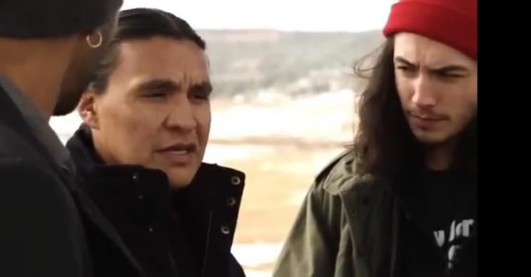 Chase Iron Eyes in a red hat speaking with Ezra Miller