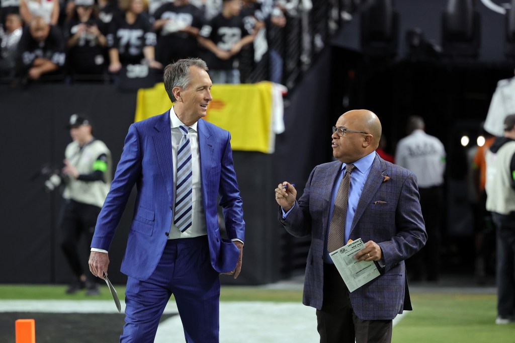 Sunday Night Football color commentator Cris Collinsworth (L) and play-by-play announcer Mike Tirico walk onto the field before a game between the New York Jets and the Las Vegas Raiders at Allegiant Stadium on November 12, 2023 in Las Vegas, Nevada. 