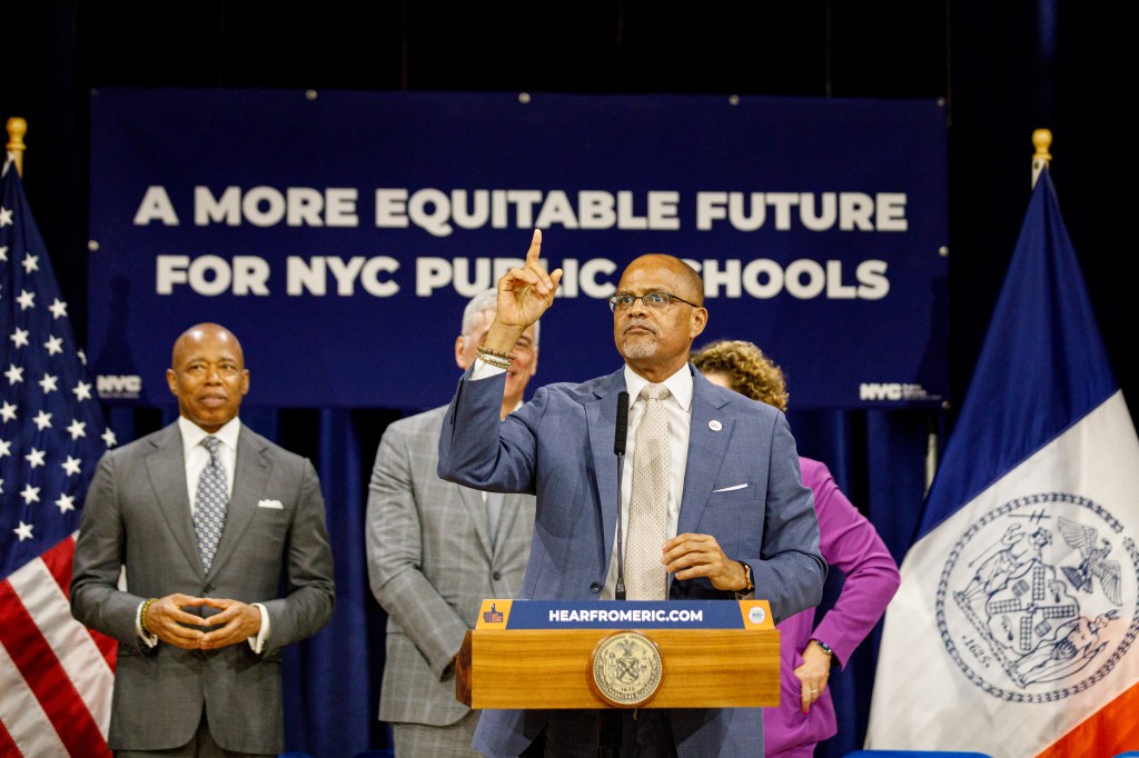 New York City Department of Education Chancellor David C. Banks speaking at a press conference about building a more equitable future for NYC public schools, pointing up while standing at a podium.