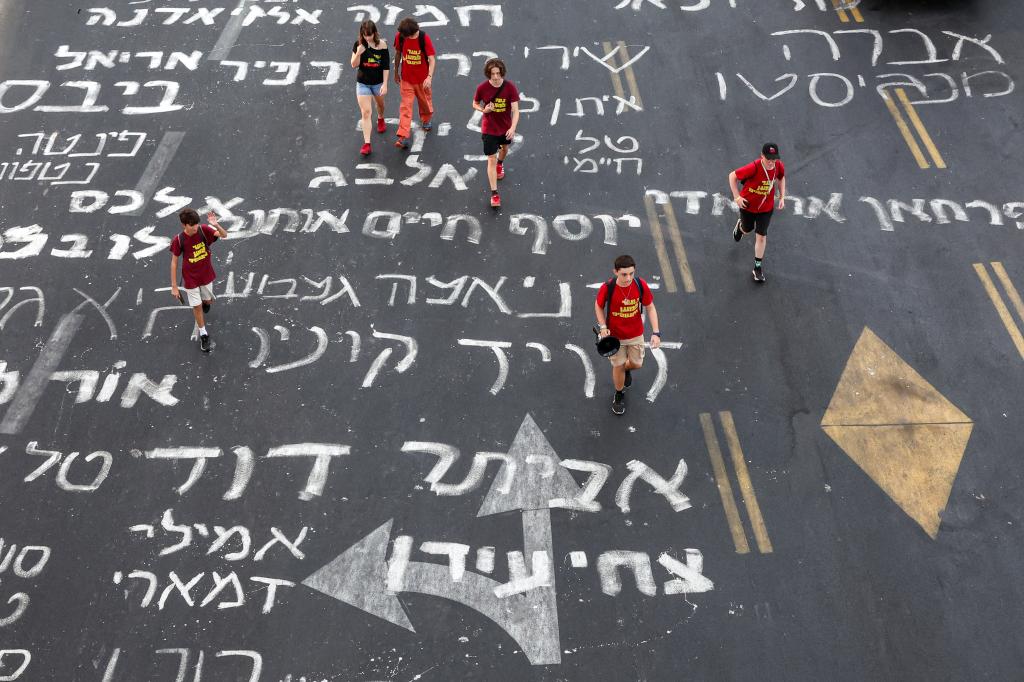 Young demonstrators wearing red t-shirts walk along a road inscribed in Hebrew with the names of Israeli hostages captive in the Gaza since the Oct. 7 attacks. 