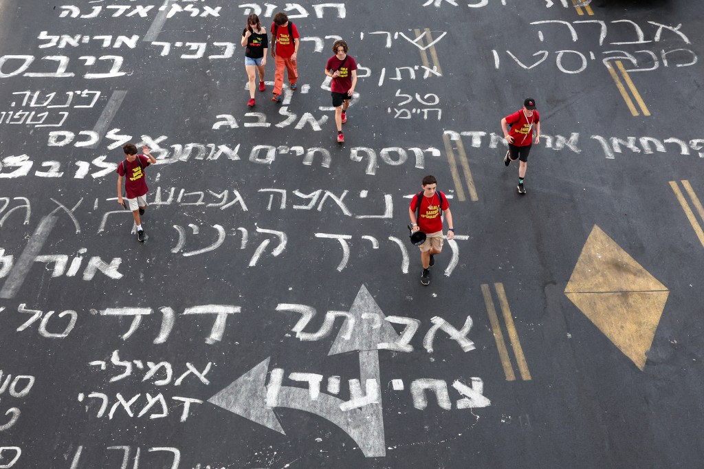 Young demonstrators wearing red t-shirts walk along a road inscribed in Hebrew with the names of Israeli hostages captive in the Gaza since the Oct. 7 attacks. 