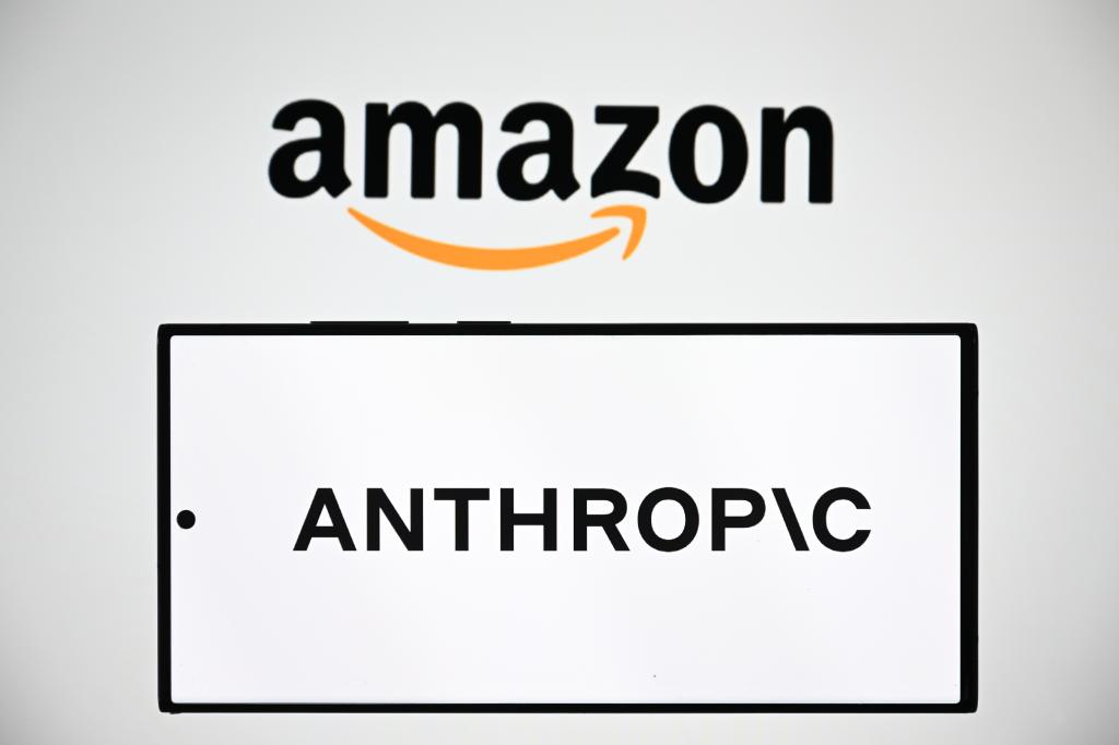 Mobile phone displaying Anthropic logo in foreground with Amazon logo visible on computer screen in background.