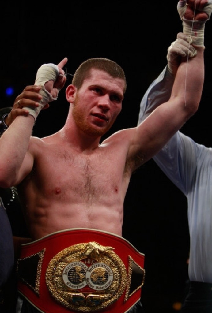 Dmitriy Salita, shirtless, wears a gold champion belt and holds his hands up in victory.