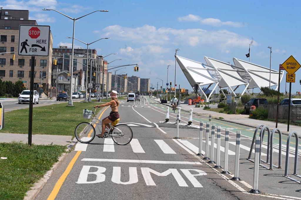 A woman riding a bicycle near the Beach 94th Street Amphitheater in Rockaway Beach, Queens, surrounded by residential real estate