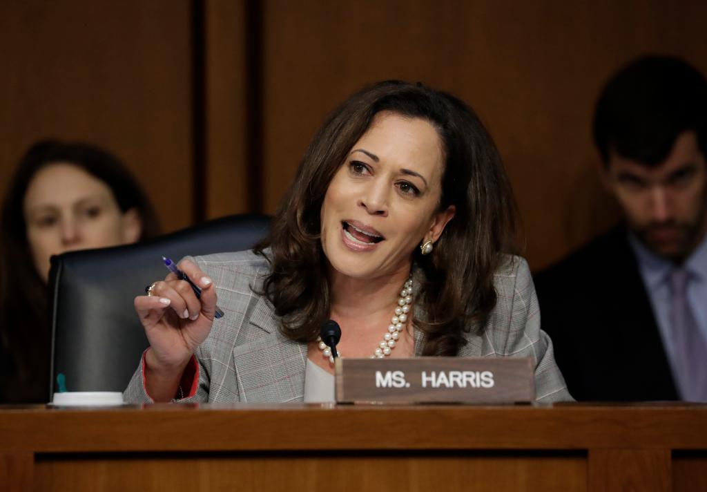 Senator Kamala Harris questioning Attorney General Jeff Sessions at a Senate Select Committee meeting, with a sign and microphone on the desk