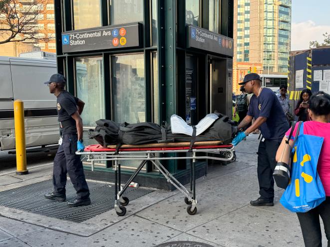 Authorities roll a body bag on a stretcher past a subway elevator.