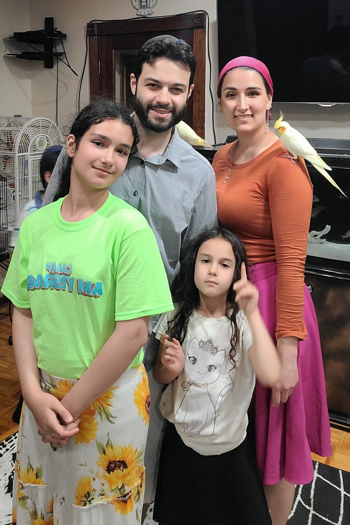 Two parents, each with a cockatiel on a shoulder, stand behind two girls.