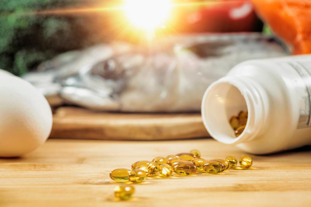 Vitamin D supplement bottle with gel capsules on a wooden table, natural food sources of Vitamin D in the background