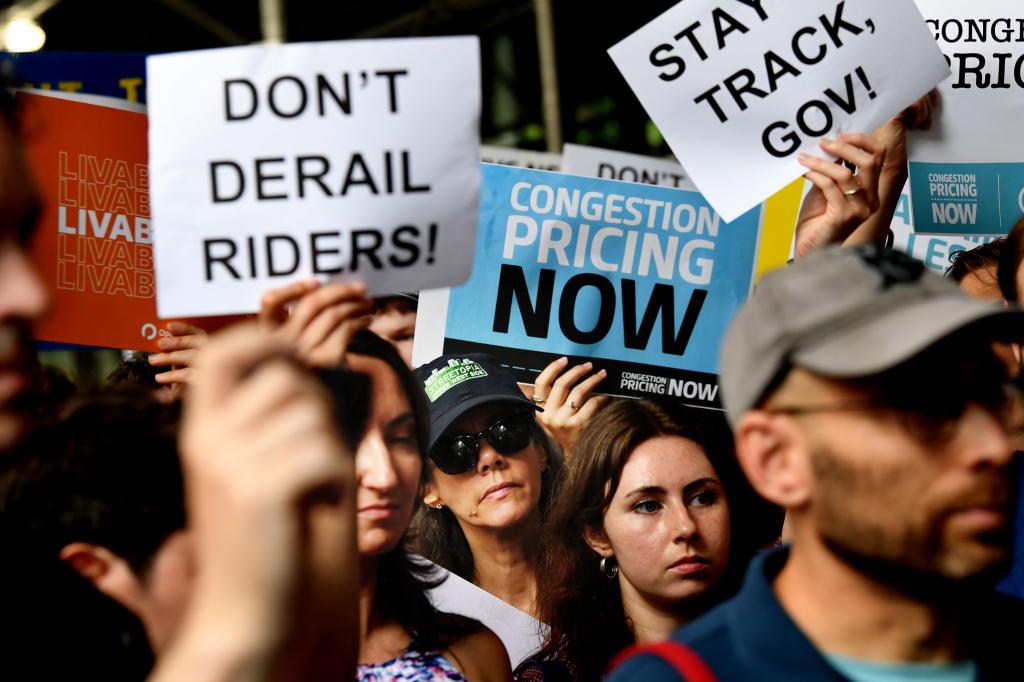 Local leaders and supporters protesting outside NY Governor Kathy Hochul's office against the delay in Congestion Pricing implementation, holding signs in disagreement