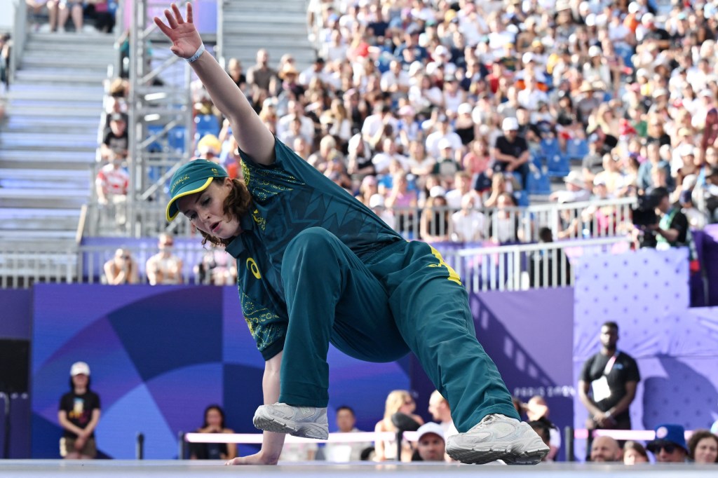 B-Girl Raygun of Australia performing at the Paris 2024 Olympics, dancing on stage in a green outfit with an audience in the background