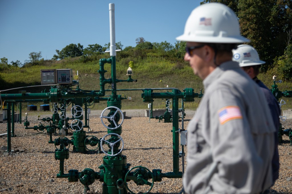 A roughneck stands in front of an oil well