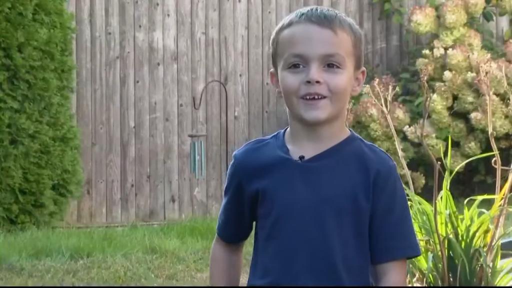 Young boy speaking to camera in a suburban backyard.