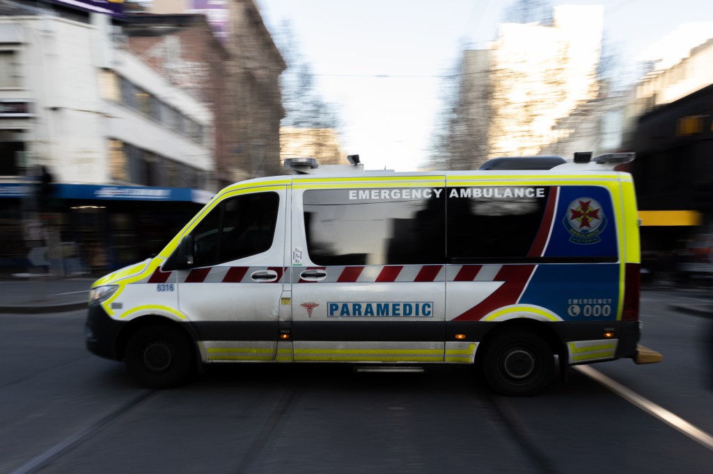 An ambulance driving through Melbourne's CBD amidst rising COVID-19 cases and hospital admissions