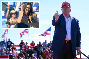 Donald Trump in a suit and a red hat giving a thumbs up with Kamala Harris in the background