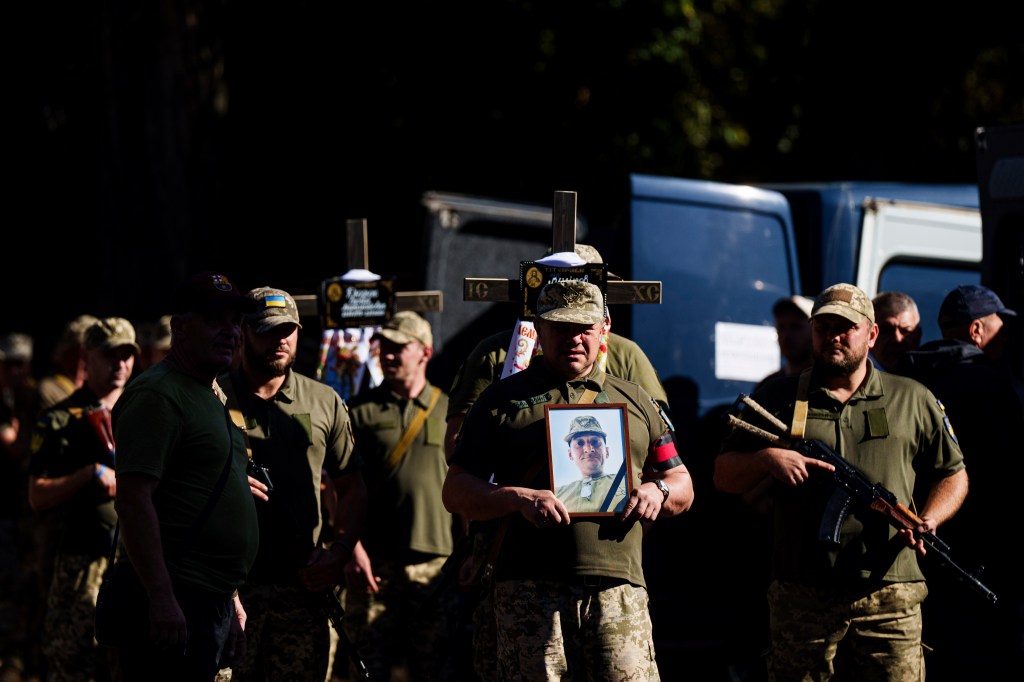 Ukrainian servicemen holding crosses and pictures of fallen comrades during a funeral ceremony in Poltava, Ukraine