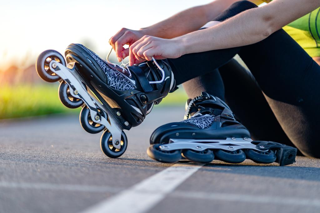 A teenager girl outdoors, lacing her roller skates for inline skating.