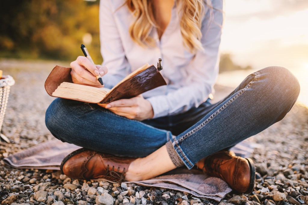 Cropped picture of focused fashionable beautiful caucasian woman sitting near river and holding notebook.