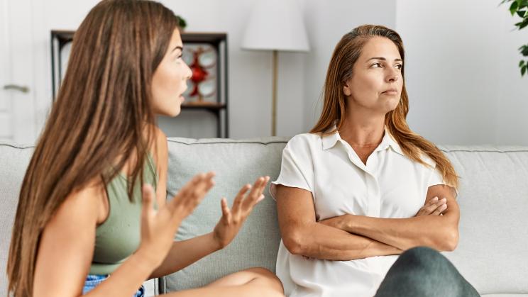 Mother and daughter arguing with unhappy expressions while sitting on a sofa at home