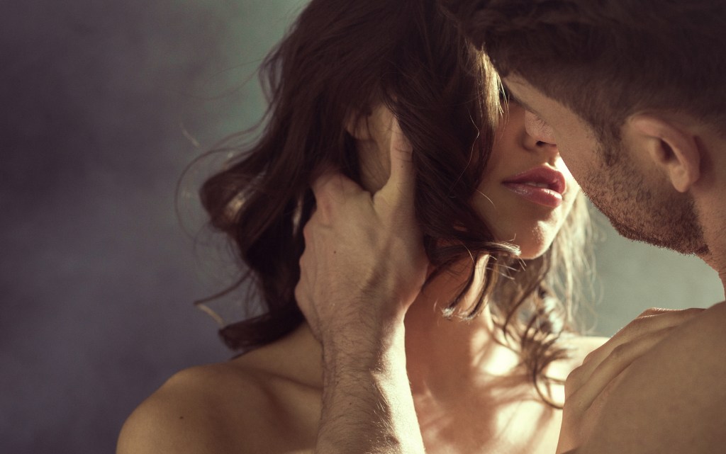 Sensual woman passionately kissing her handsome husband, with the man tenderly holding her face