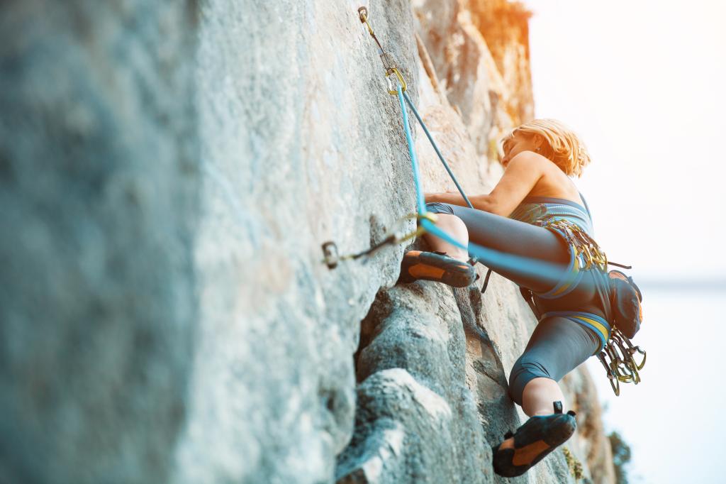 Adult female rock climber scaling a vertical flat wall, side view