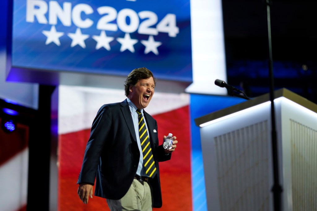 Tucker Carlson laughing while speaking at the podium during the 2024 Republican National Convention in Milwaukee