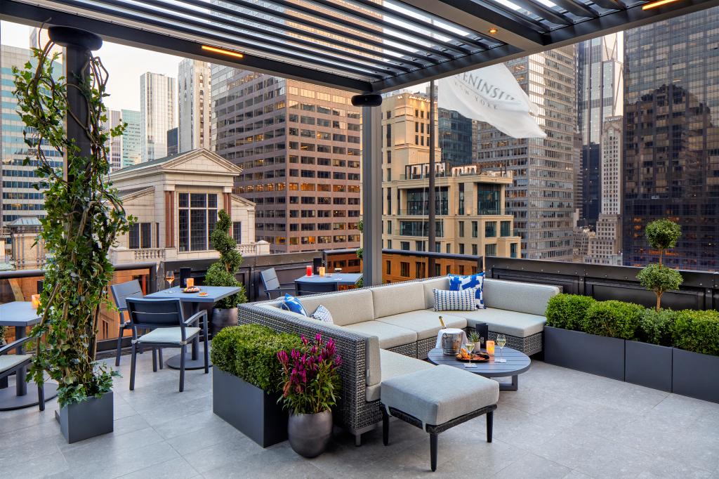 A patio with a large couch, tables, and chairs on a rooftop
