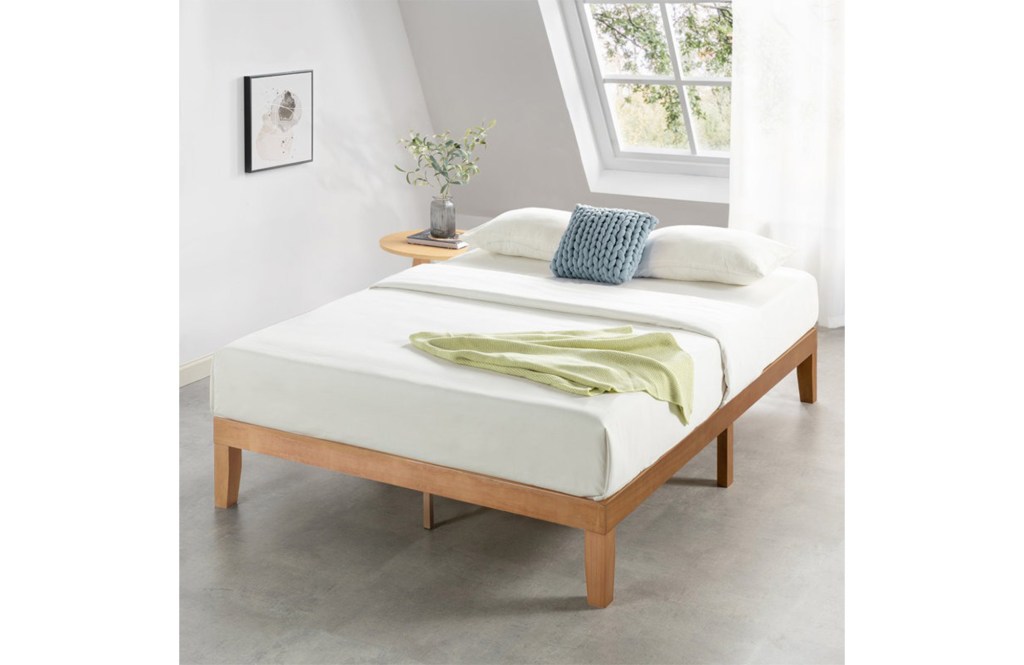 A wooden bed frame with an adjacent table holding a plant