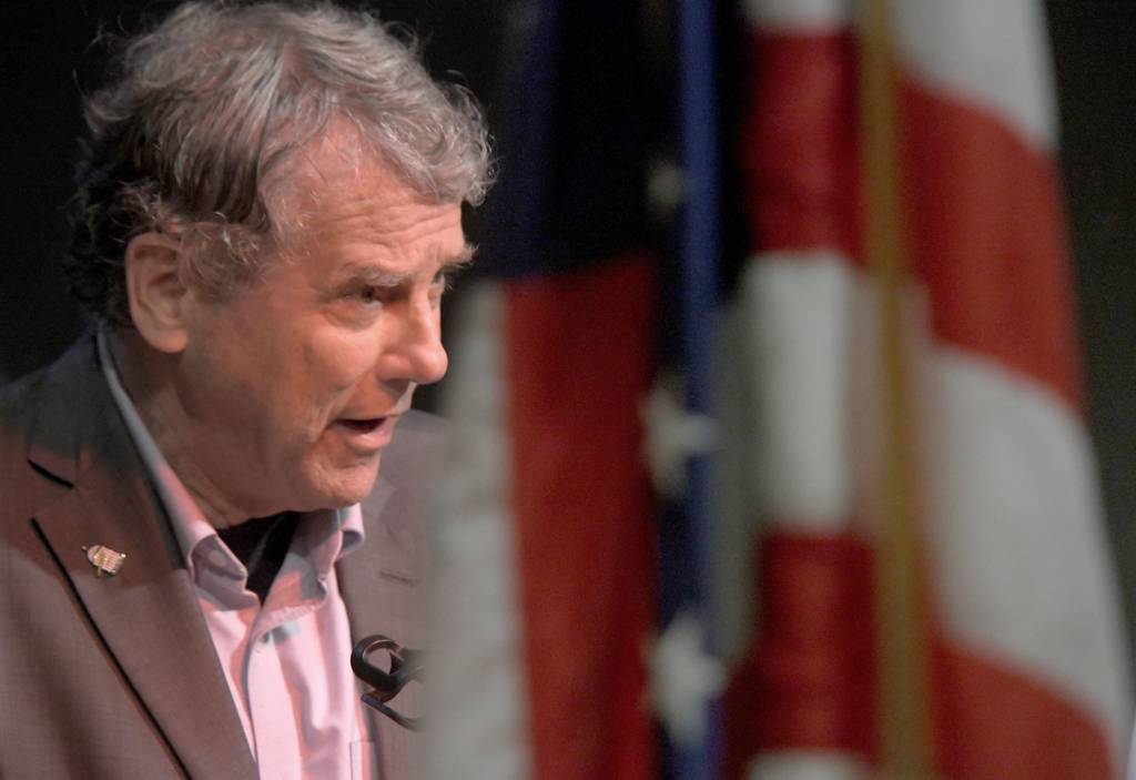 Senator Sherrod Brown speaking into a microphone at the AMVETS Post 26 about the All-American Flag Act