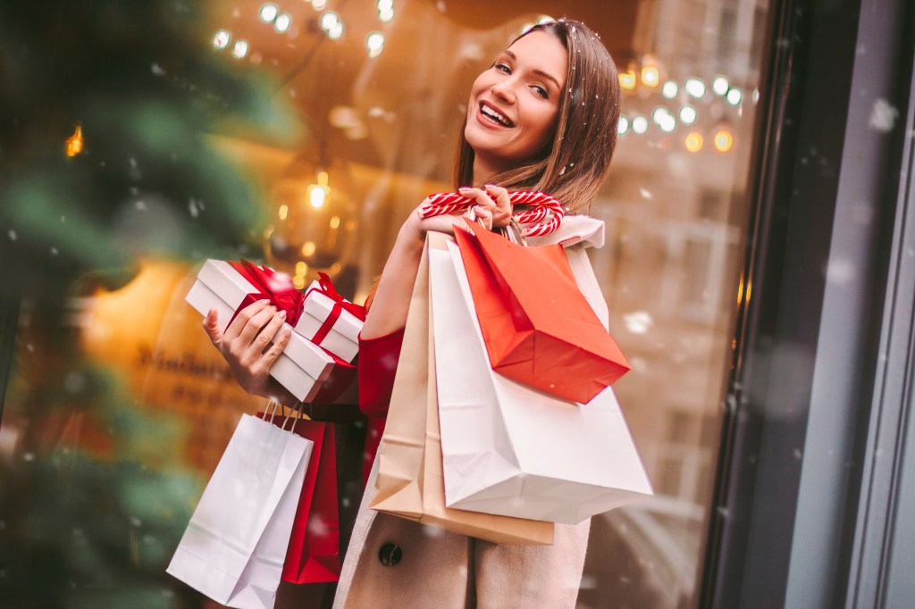 A happy woman smiling and holding shopping bags and gift boxes in a city street after Christmas shopping.