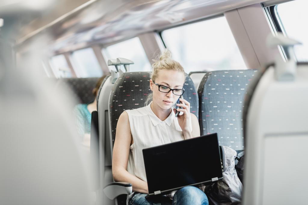 Businesswoman on train, talking on cellphone and working on laptop