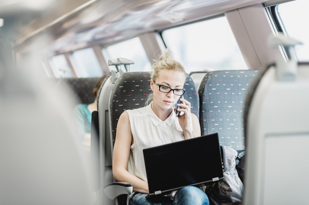 Businesswoman on train, talking on cellphone and working on laptop