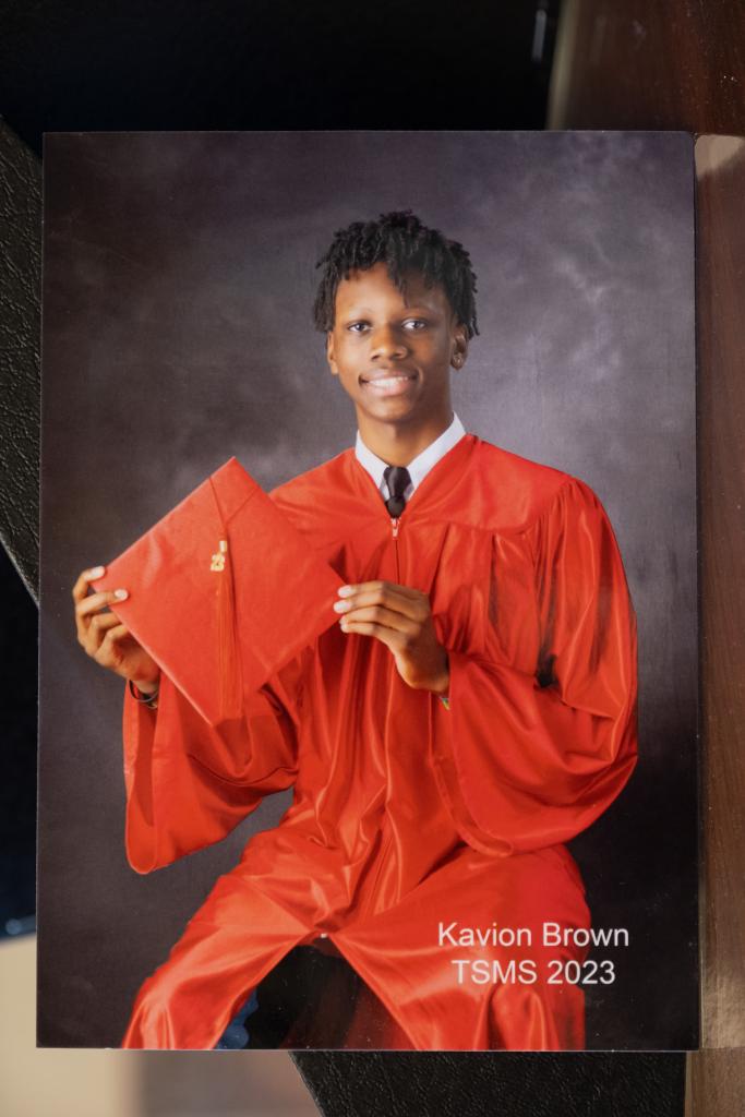 Kavion Brown Godfrey in red graduation robes holding his hat.