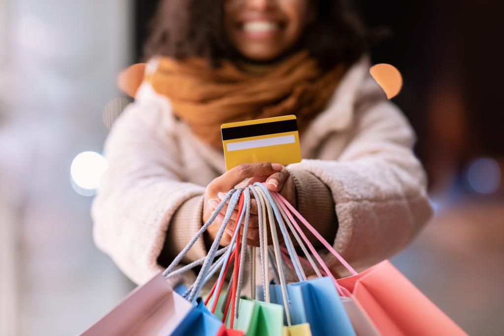 Closeup Of Unrecognizable Black Woman In Winter Coat Showing Credit Card, Holding Bright Colorful Shopping Bags.