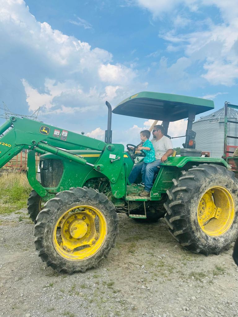 Pennsylvania farmer Ben Logan with small child on large green John Deere tractor.