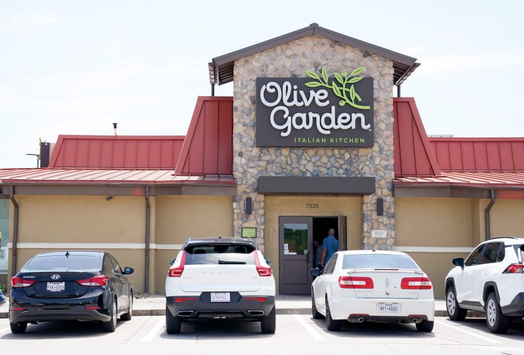 Exterior view of an Olive Garden restaurant with cars parked in front, in Houston, TX.