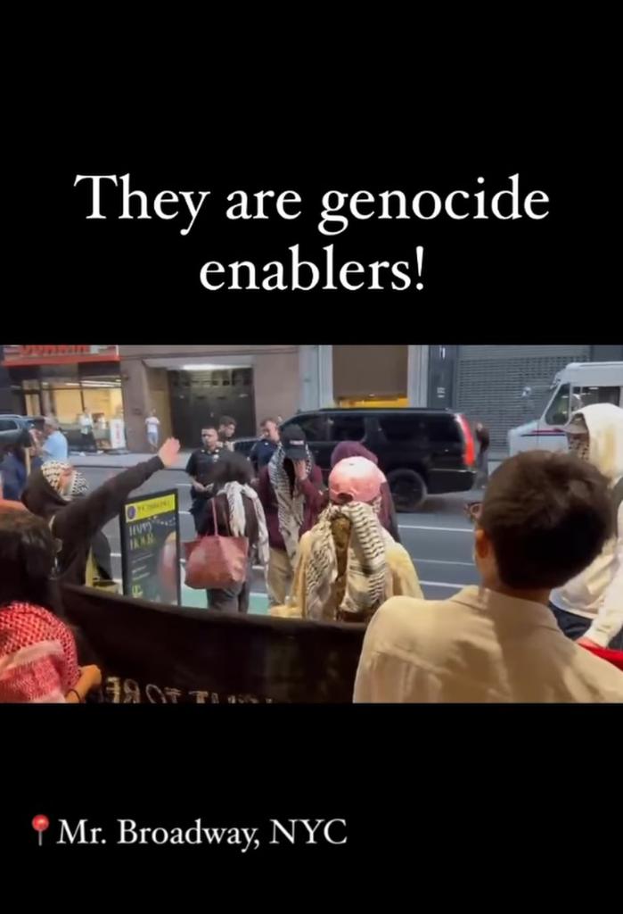 Screenshot from video showing protest outside Hillel dinner in midtown, young people seen with keffiyehs and a banner, subtitle of chants reading "They are genocide enablers!"