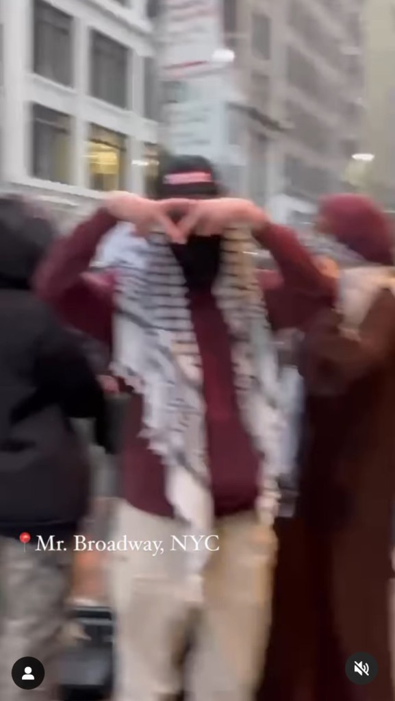 Screenshot from protest video showing one man in keffiyeh, hat and sweatshirt flashing upside-down triangle symbol with his fingers.