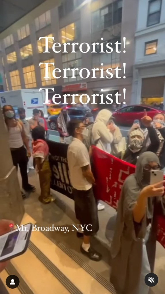 Screenshot from video taken at protest with group wearing masks and keffiyehs on sidewalk, holding protest banner and chanting "Terrorist!" with Mr. Broadway location tagged with pinpoint.