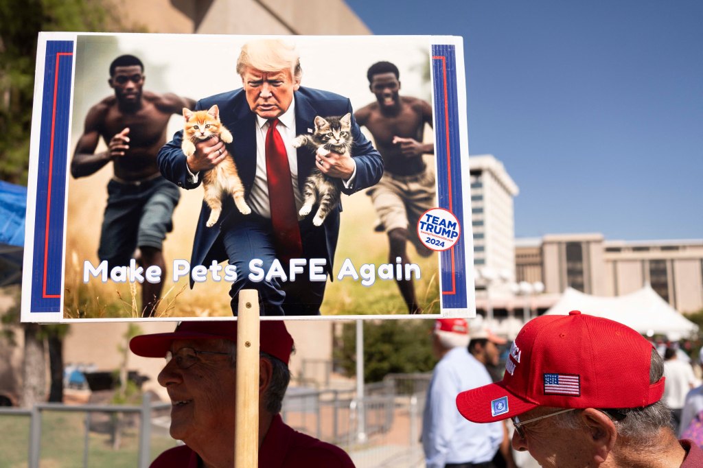 A man carries an AI-generated image of former US President and Republican presidential candidate Donald Trump carrying cats away from Haitian immigrants.