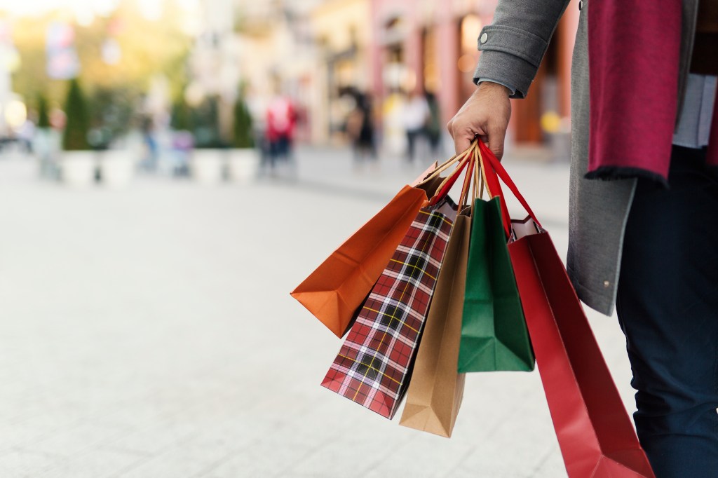 Man holding multiple shopping bags with presents on a city street.