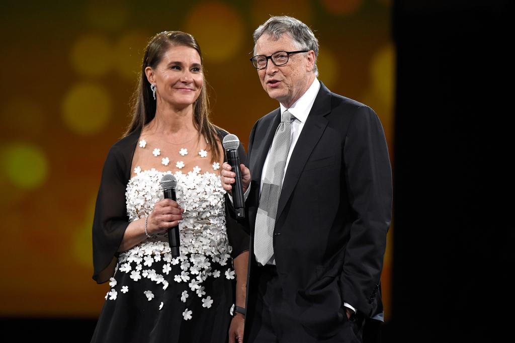 Bill Gates and Melinda Gates speaking on stage with microphones at The Robin Hood Foundation's 2018 benefit in New York City.