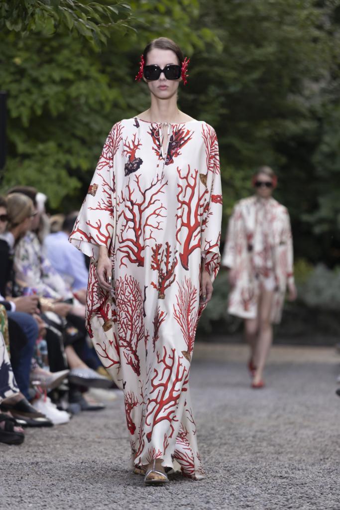 A model wearing a long white dress with red corals, presenting a Libertine creation at a New York Fashion Week show.