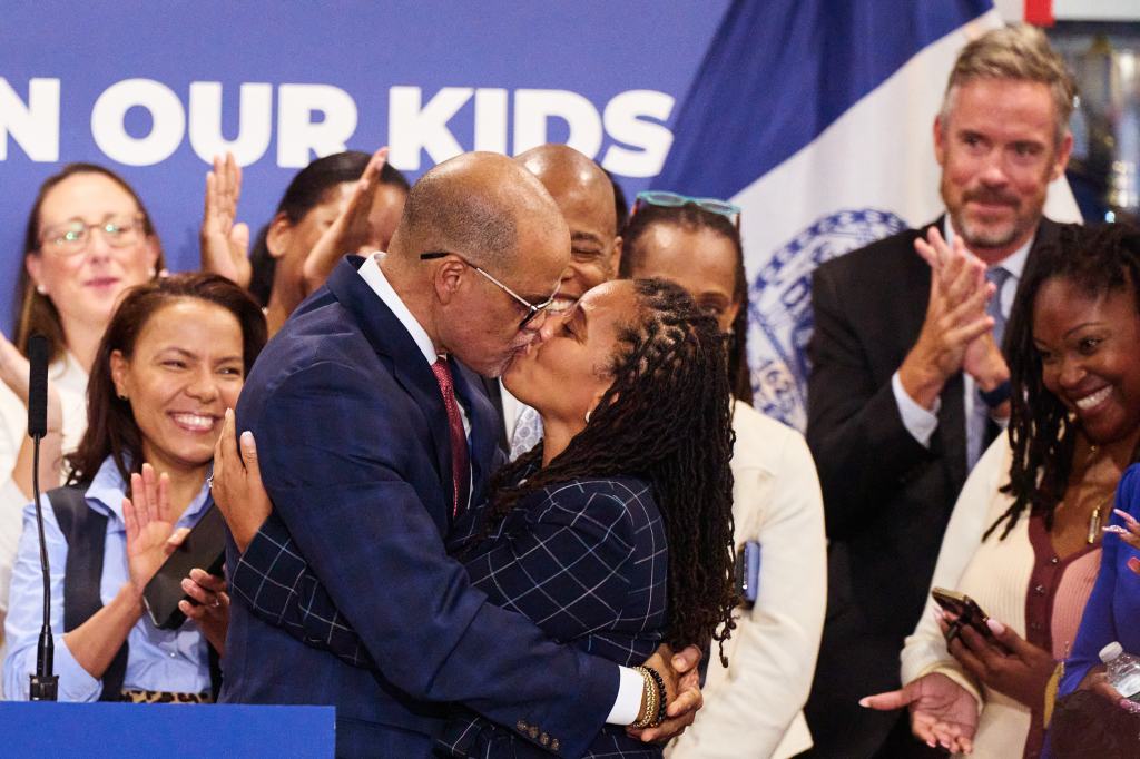 New York City Schools Chancellor David Banks embracing First Deputy Mayor Sheena Wright, with Mayor Eric Adams observing during news conference