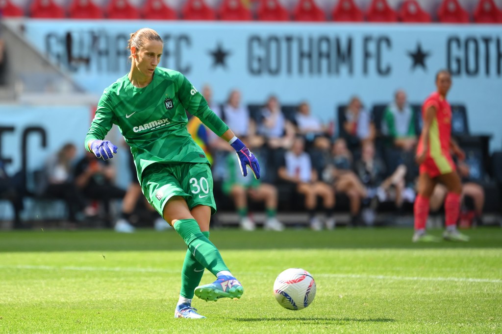 NJ/NY Gotham FC goalkeeper Ann-Katrin Berger in green uniform, kicking a soccer ball during a match against Portland Thorns FC at Red Bull Arena.