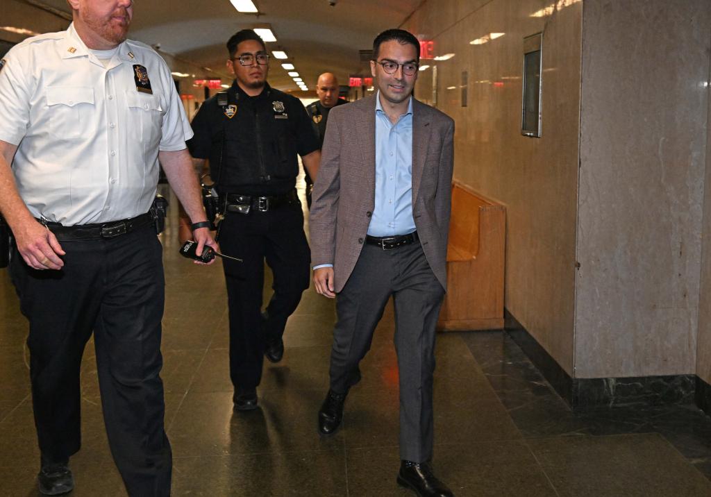 Eric Ulrich, former Commissioner of Buildings, in a brown sports jacket, walking down a hallway in court with police officers