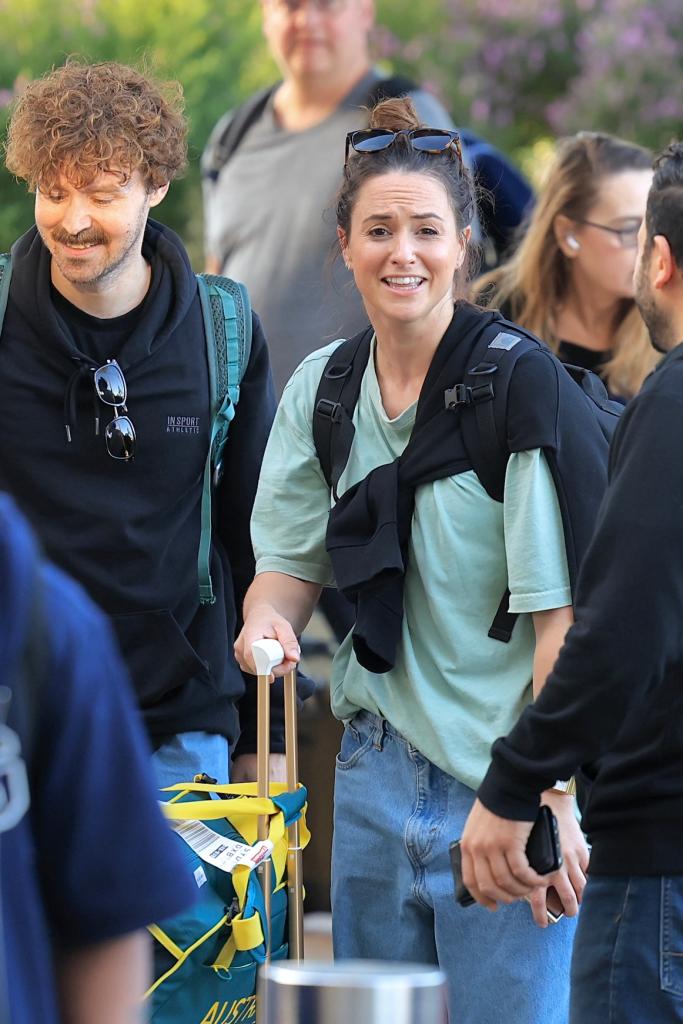 Rachael 'Raygun' Gunn and her husband Samuel Free arriving at Sydney International Airport with their luggage and Team Australia sports bag, smiling with an Uber in the background