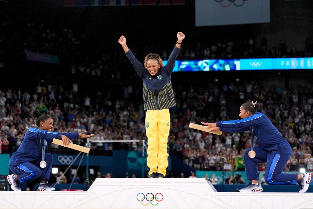 Silver medalist Simone Biles, of the United States, left, and Jordan Chiles, of the United States, right, bow to gold medalist Rebeca Andrade, of Brazil, during the medal ceremony for the women's artistic gymnastics individual floor finals at Bercy Arena at the 2024 Summer Olympics.