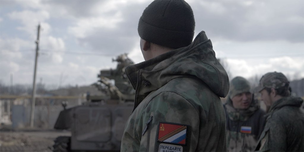 A still from director Anastasia Trofimova's movie "Russians at War," which shows showing a man in a military jacket seen from behind during wartime.